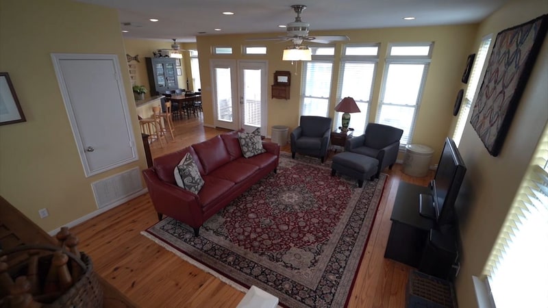 Khung hình từ video John Reynolds với sofa đỏ, hai ghế và cầu thang trong phòng khách.